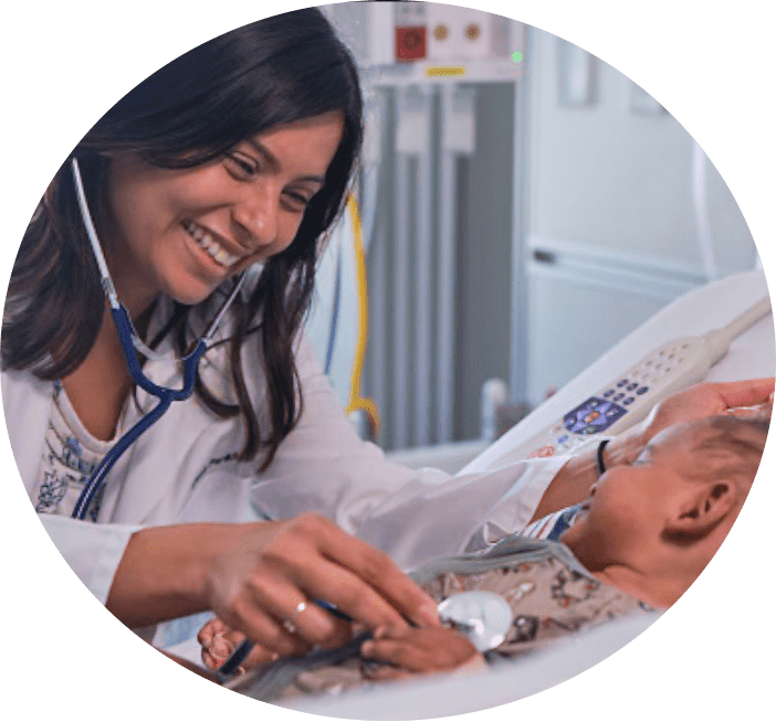 female physician smiling at a baby in a hospital bed while placing a stethoscope on its chest.