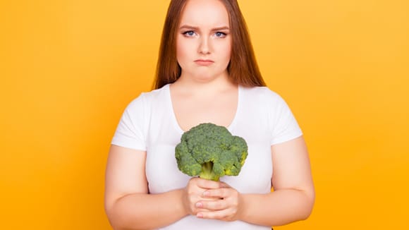 Girl looking sad holding a stalk of broccoli