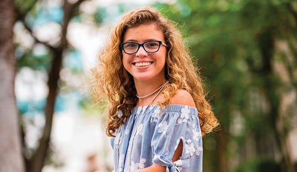 young woman smiling in front of trees