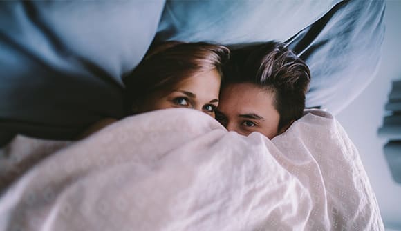 A couple under the covers looking sneaky