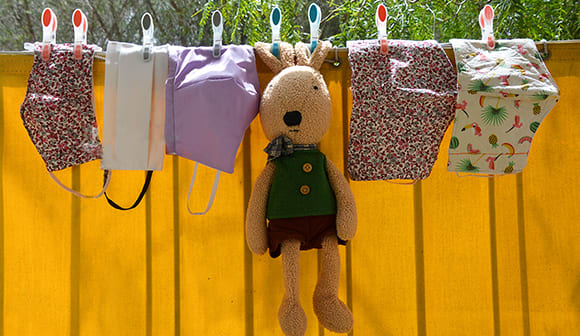Cloth face masks and a stuffed animal hanging on a clothes line.
