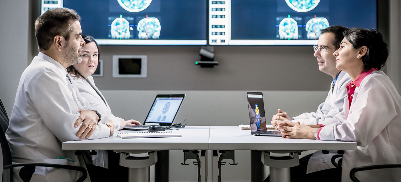 A group of brain and spine tumor specialists gather in front of a patient's brain scans at the weekly tumor board.