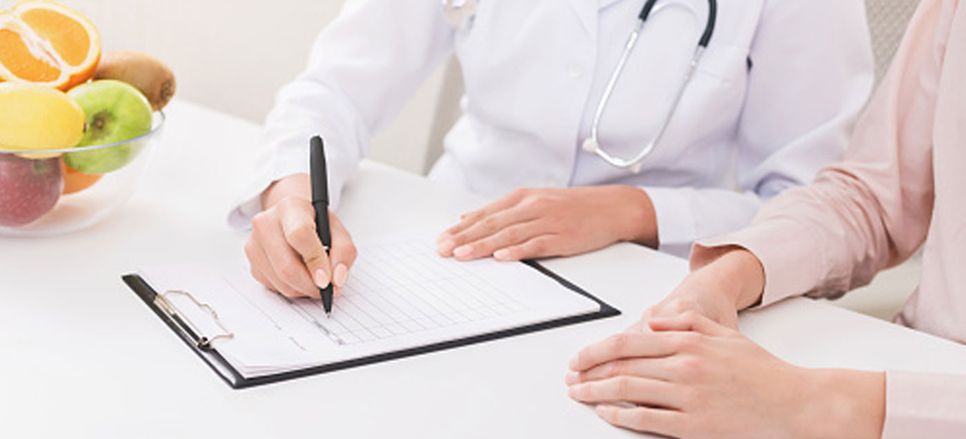 A cropped shot of two women's hands, one going through a clipboard form, and a bowl of fruit beside them.