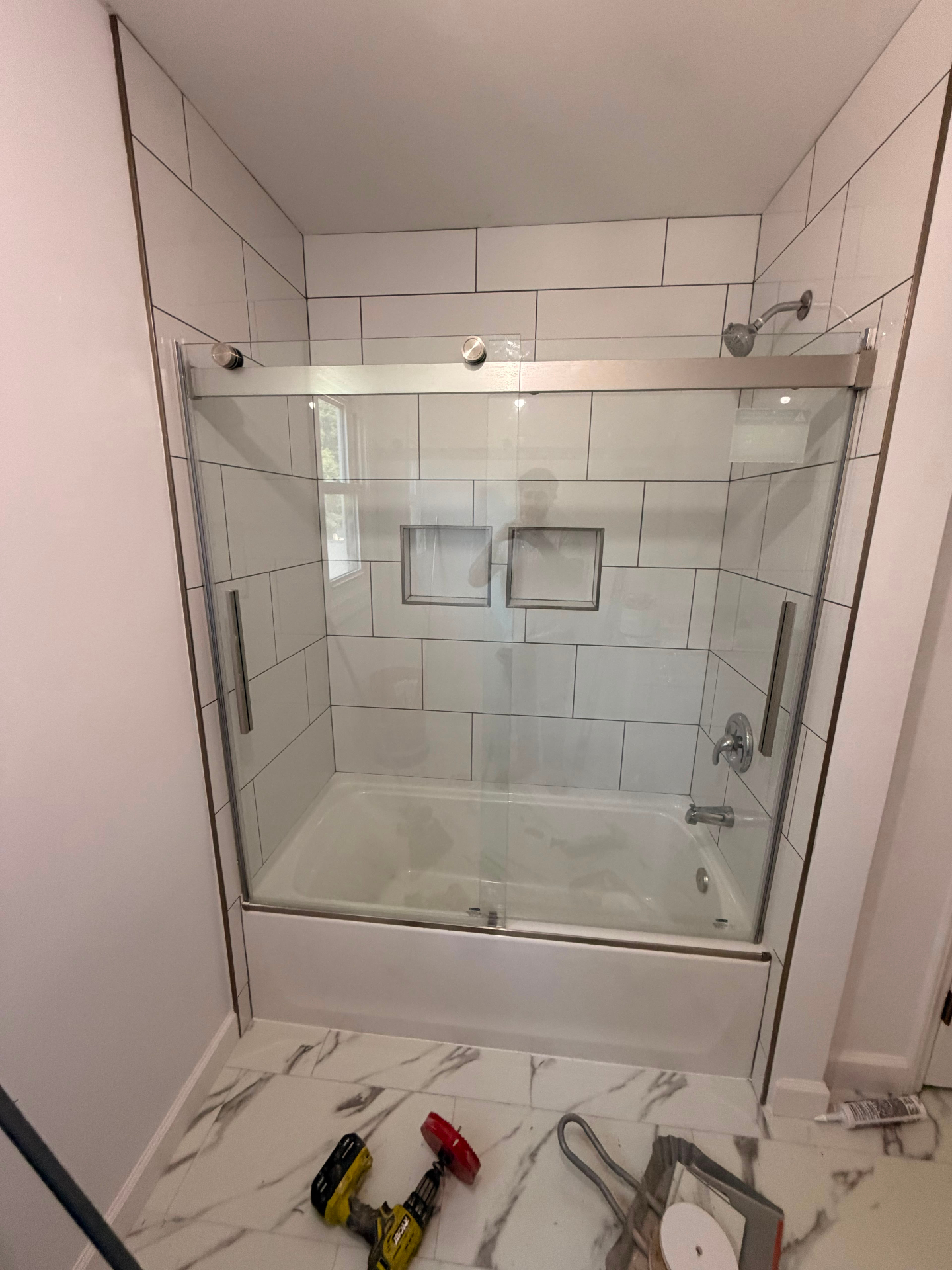 Finished bathroom with large white tile surround, custom niche, and glass shower doors