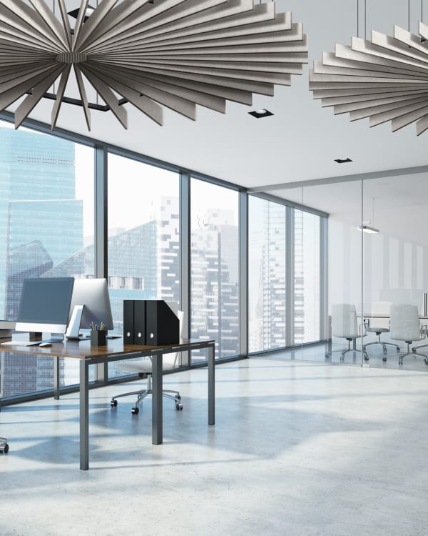 Modern office interior with Zintra Baffles Quarter Circle acoustic panels installed on the ceiling. The image shows two circular arrangements of the baffles, creating a decorative and functional ceiling design. A large window with a cityscape view is visible, along with office furniture including desks, chairs, and computers.