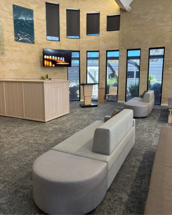 Botton + Gardiner Atomik modular seating in a light textured fabric with an integrated ottoman, complementing the light timber lectern and flower pedestal in a modern service room at Geelong Memorial Park & Crematorium.