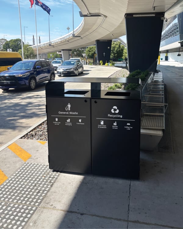 Black botton+gardiner Bondi Bin Double waste and recycling station with clear white graphics for General Waste and Recycling, positioned outdoors at Melbourne Airport (MEL).