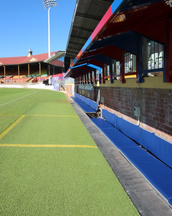 An outdoor stadium sideline view of Norwood Oval in South Australia featuring long rows of botton+gardiner Avenue cantilevered player benches upholstered in durable Baresque vinyl.