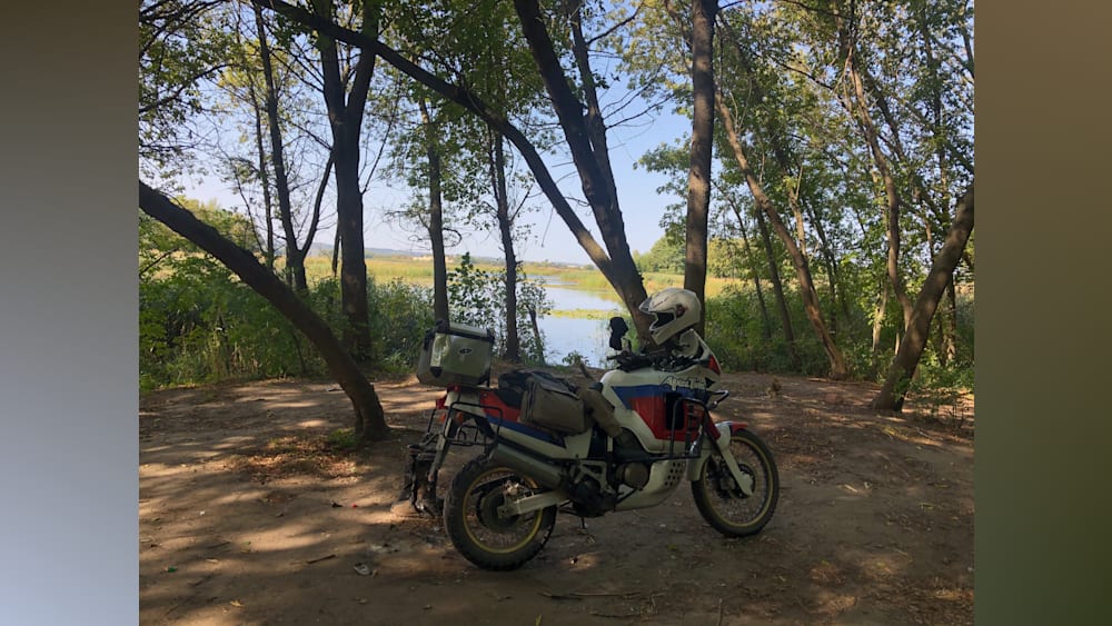 A person is taking a picture of a motorcycle parked next to a lake.