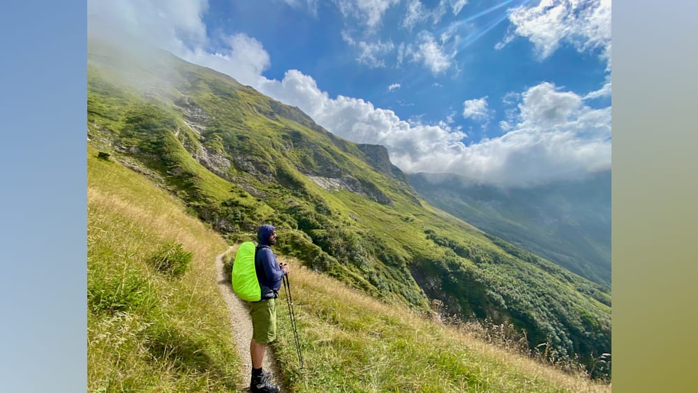 A man with a green jacket is standing at the top of a mountain looking out over the landscape.