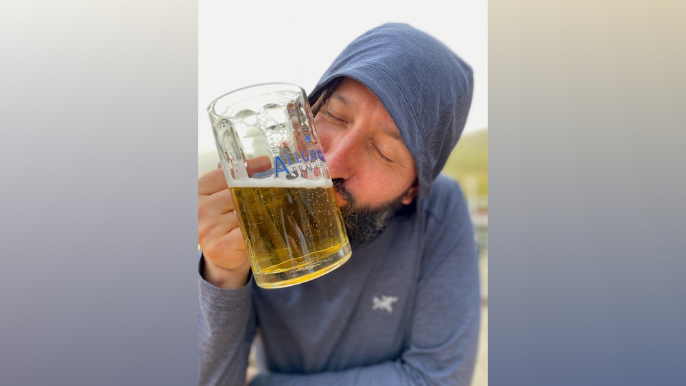 A man drinking from a large glass with the words Alligator Brand on it.