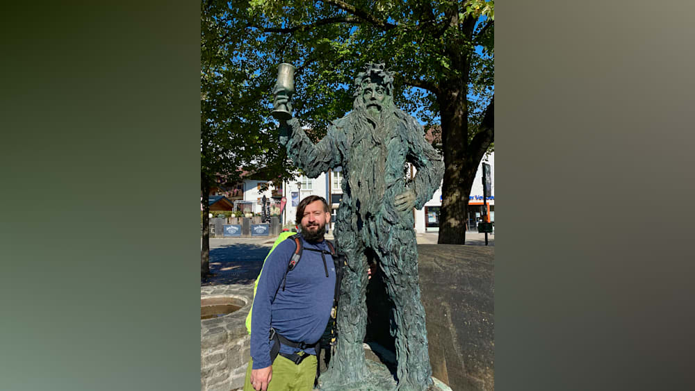 A man stands next to a statue of a giant holding a glass.