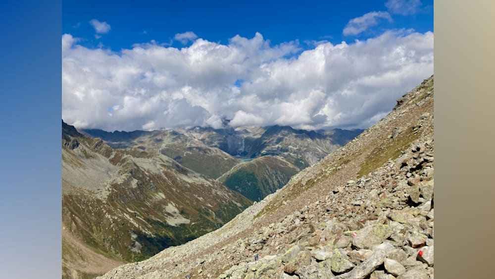 A rocky mountain side with a lake and a couple standing at the top of the mountain.
