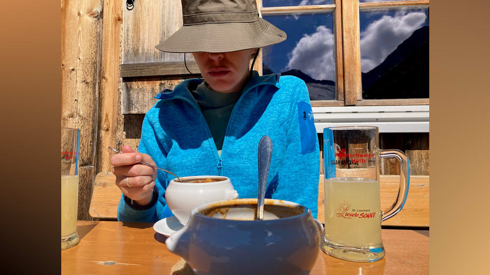 A girl in a blue jacket is sitting at a table eating soup with a spoon.