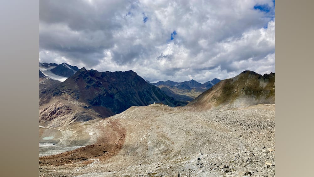 A mountain with a path in it and a large body of water in the background.