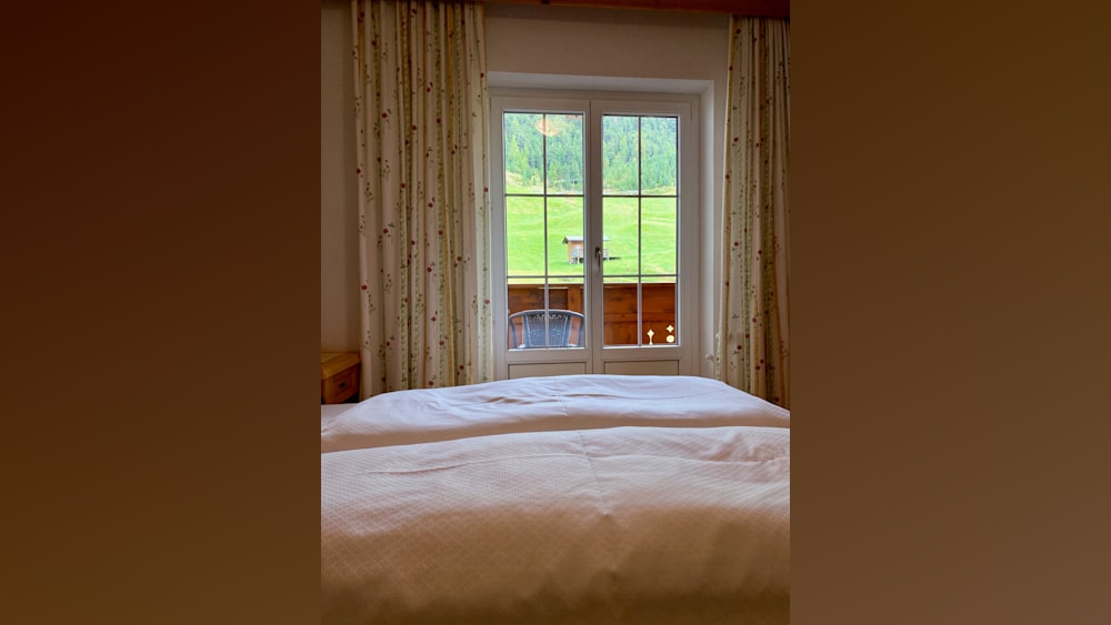 A bedroom with two made up beds and a window that looks out onto a field.