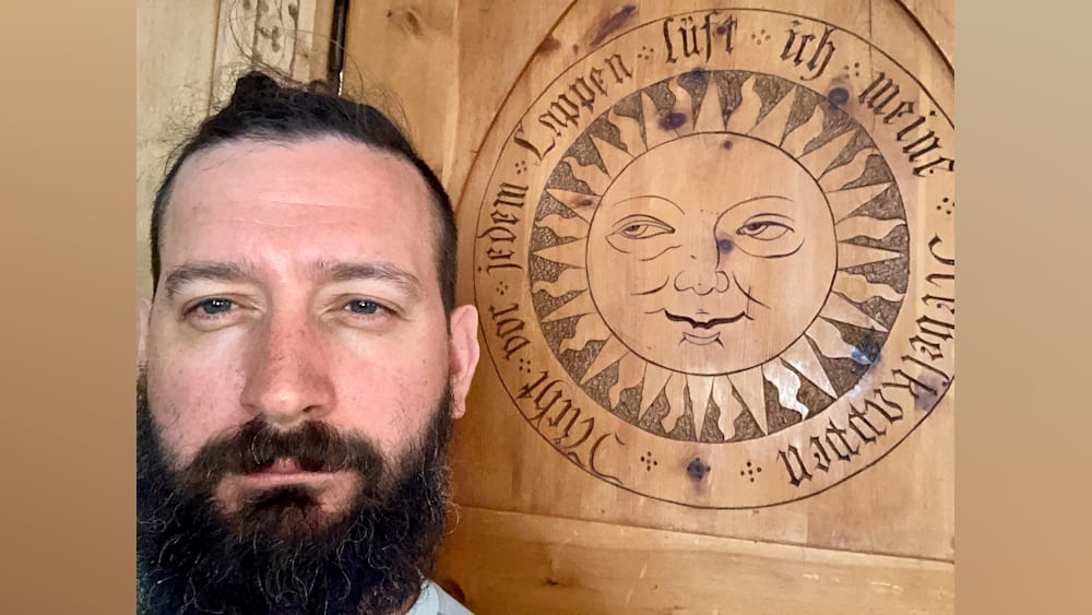 A man is looking at the camera while standing in front of a wooden sign that says "lift-i-lpoten".