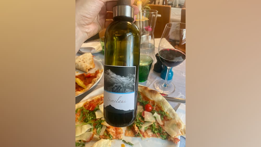 A bottle of Sinilauan wine is being held up next to a plate of pizza.