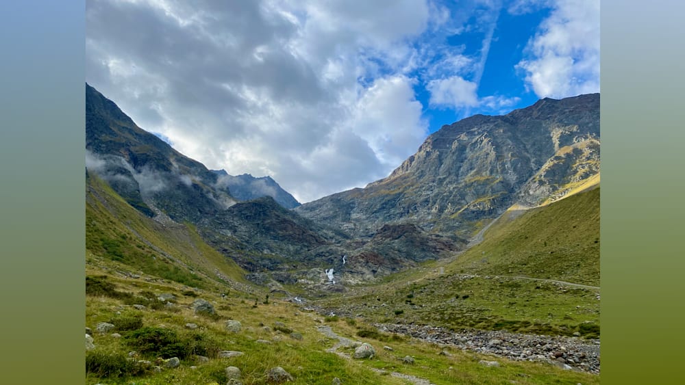 A valley with a river and a mountain with a cloud covered peak.