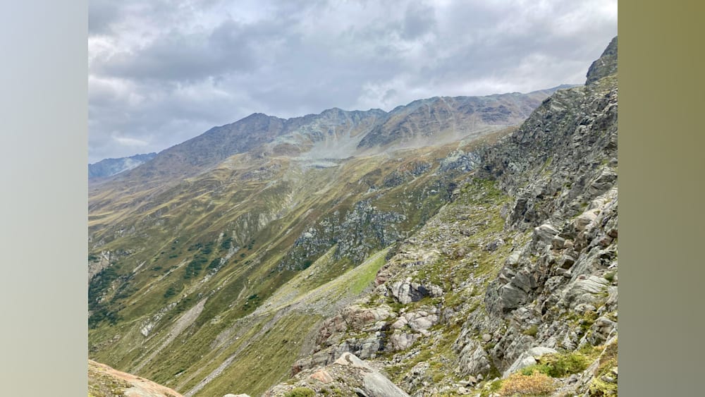 A rocky mountain side with grass and a large gray boulder in the foreground.