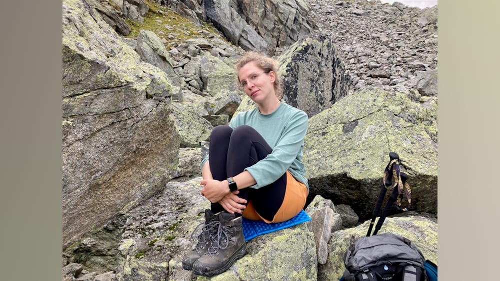 A woman sitting on a blue mat on some rocks.