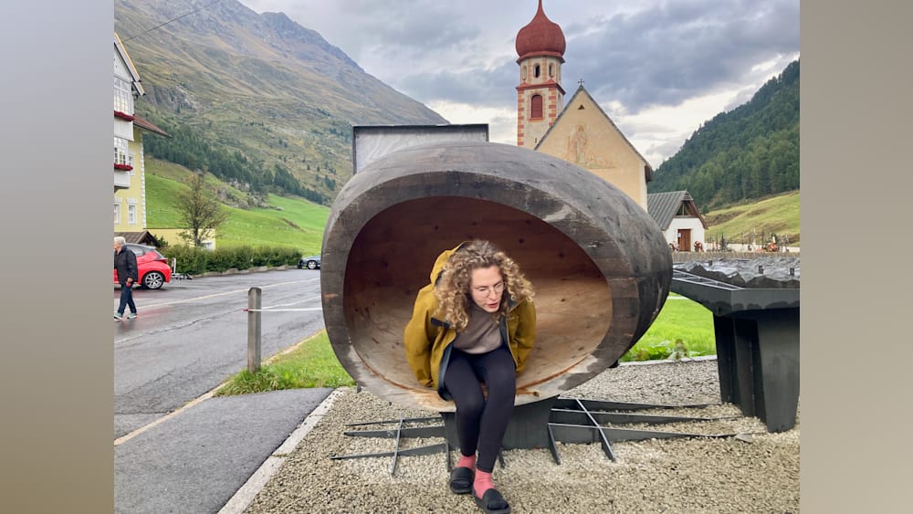 A woman in a yellow jacket sits inside a large, strange-looking bowl-like structure.