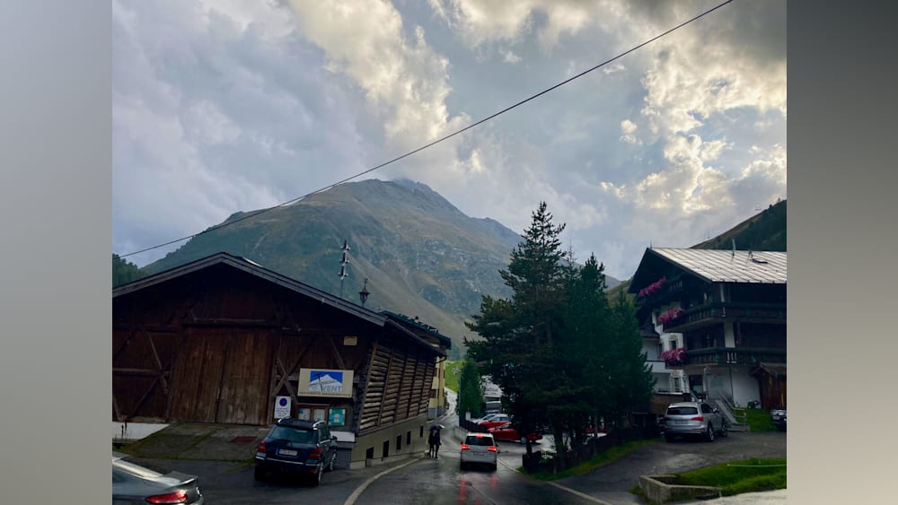 A road with cars and a building on the side of it with people walking on the sidewalk.
