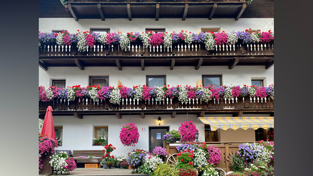The balcony of a large house is decorated with flowers in hanging baskets.