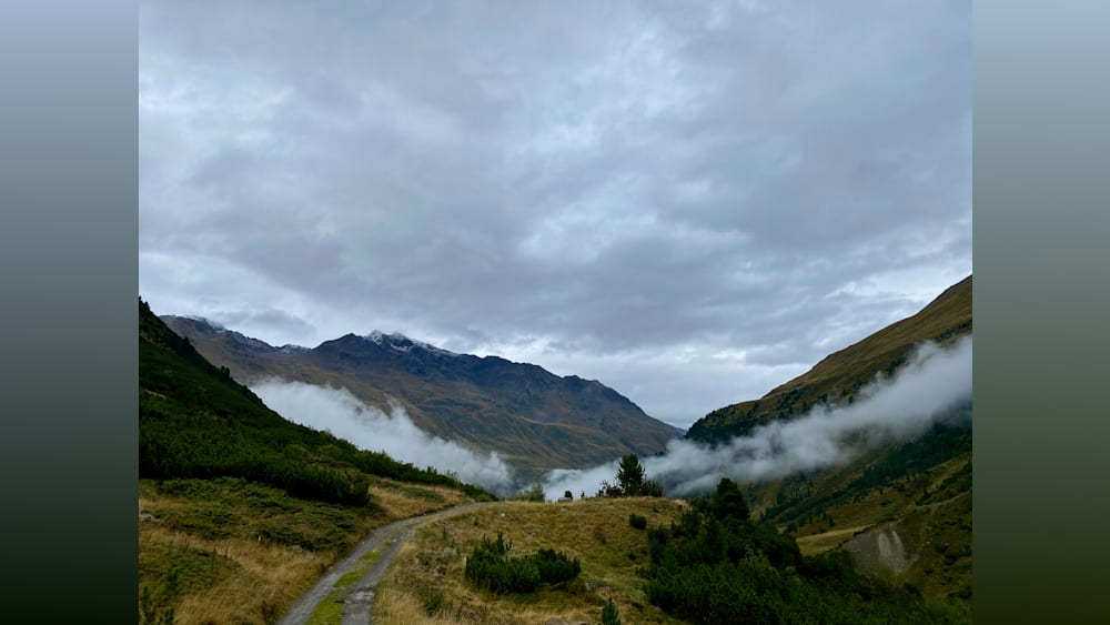 A road winds through a forest of mountains with a lot of misty mountains in the background.