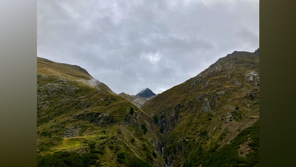 A mountain with a waterfall in the valley on a cloudy day.