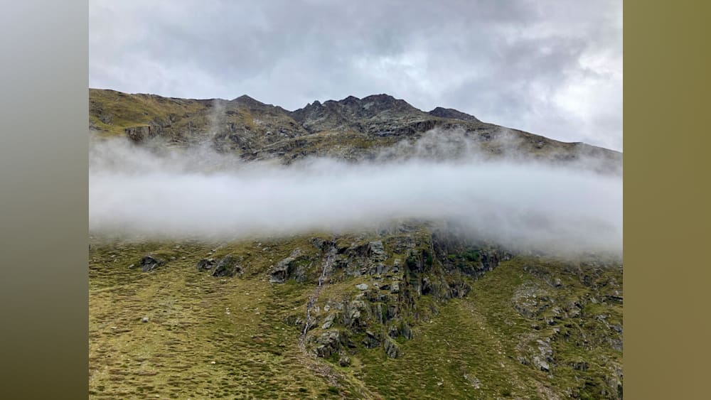 A foggy mountain with rocks on the side and a grassy area in the valley below.