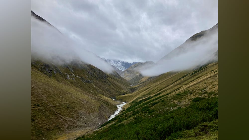 A foggy mountain range with a stream running through it.