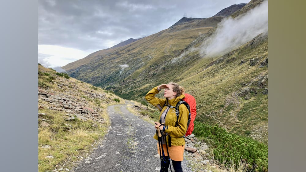 A woman in a yellow jacket looks up at a mountain.