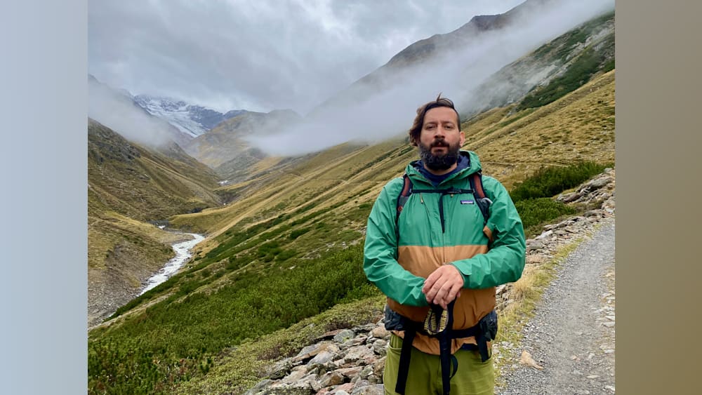 A man wearing a Patagonia jacket stands on a mountain side.