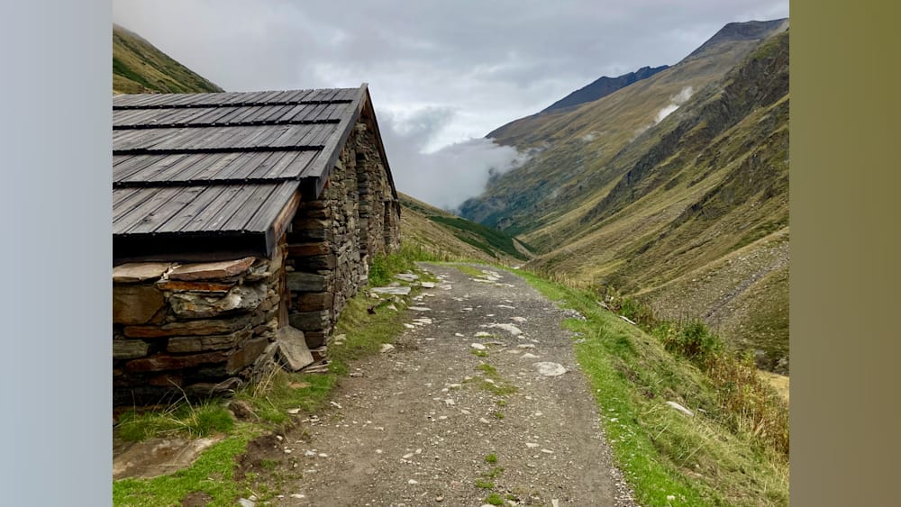 A path leads to a stone building in the mountains.