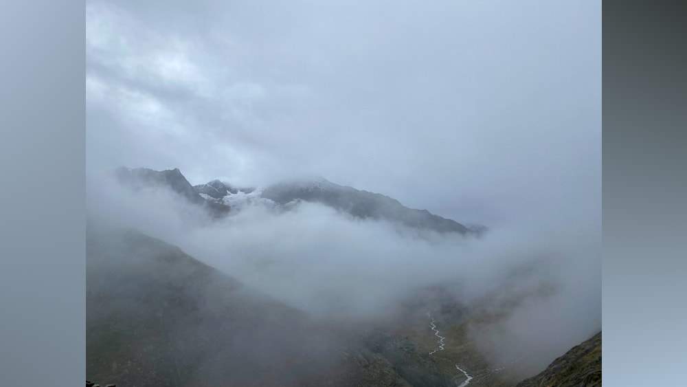 A foggy mountain with snow on the mountain and a river below.