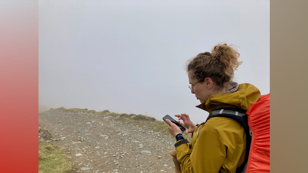 A woman looking at her phone on a rocky path.