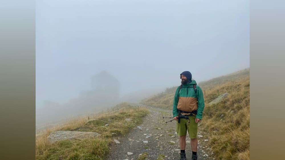 A man wearing a green jacket with brown trim is looking into the distance.