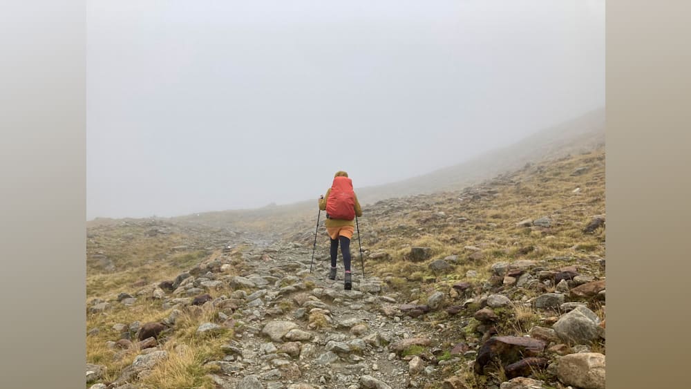 A woman hiking with a red backpack on a rocky mountain.