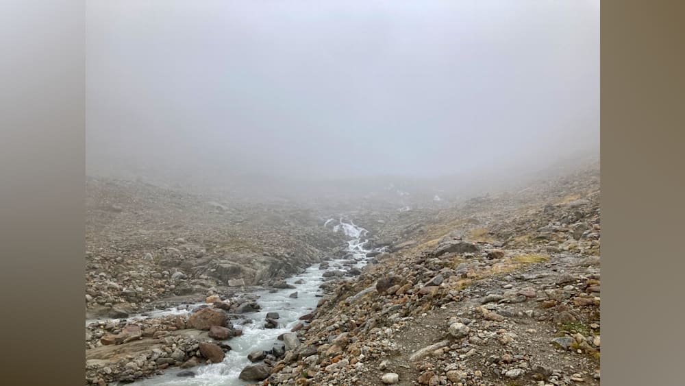 A stream of water flows down a rocky mountainside in foggy weather.