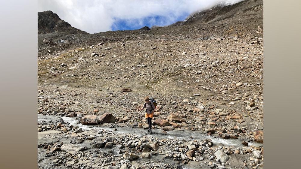 A woman is hiking and taking a picture of herself in the stream.