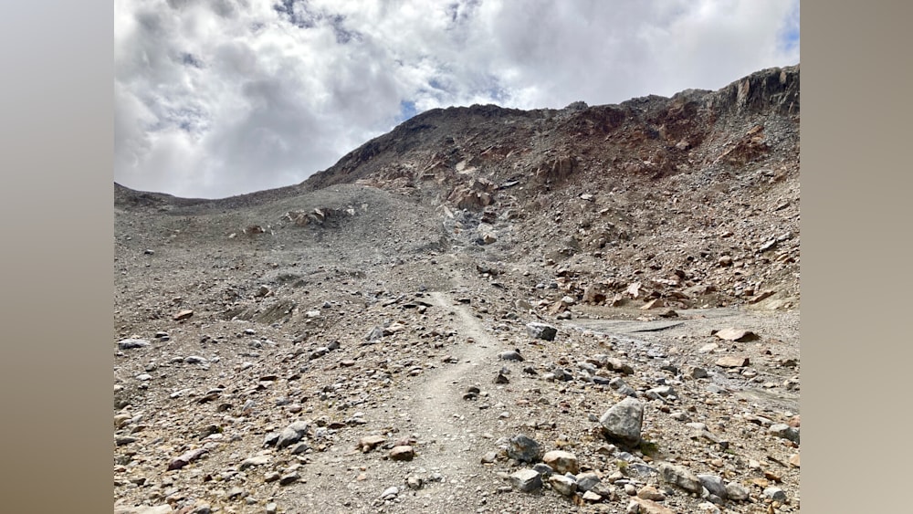 A path goes along a cliff made of boulders and sand.
