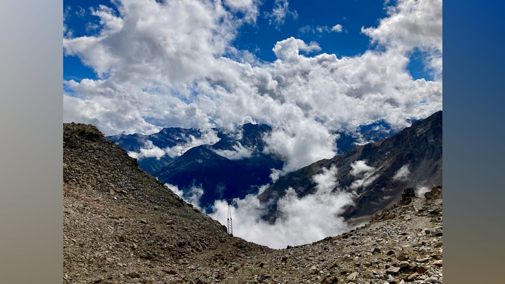 A view of a mountain from a cloud covered valley with a metal structure in the valley.