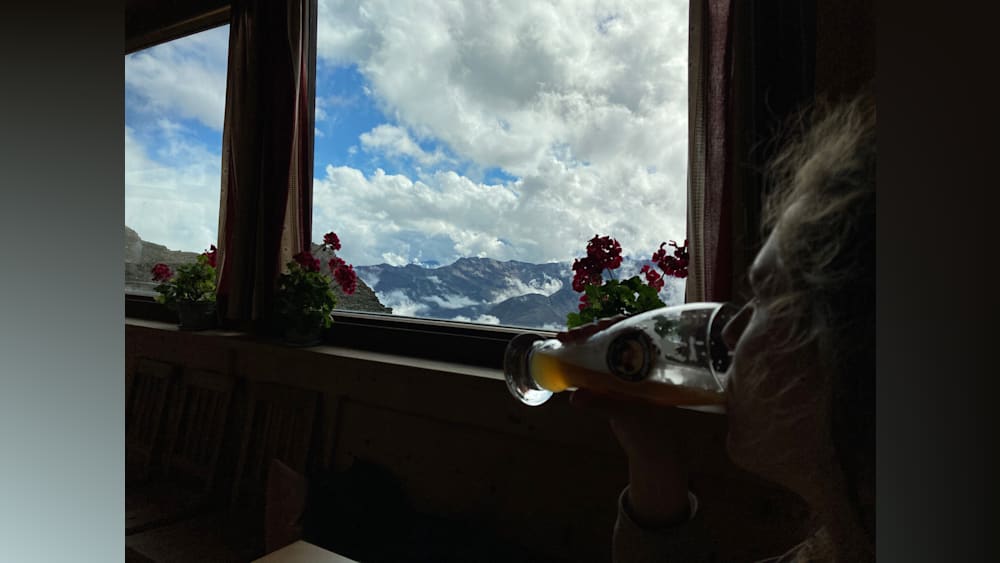 A person drinking from a bottle with a mountain range in the background.