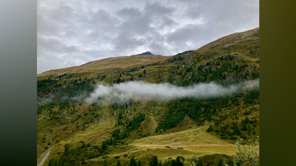 A misty mountain range with trees and grass on the slopes.