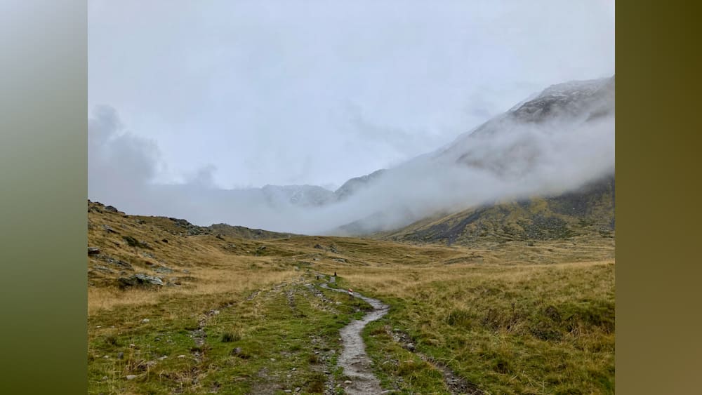 A path winds through a grassy field, between two hills, and is covered with fog.