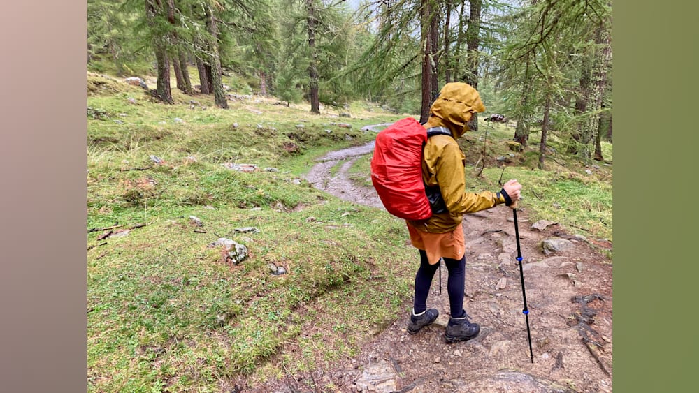 A woman with a red pack on her is walking up a hill.