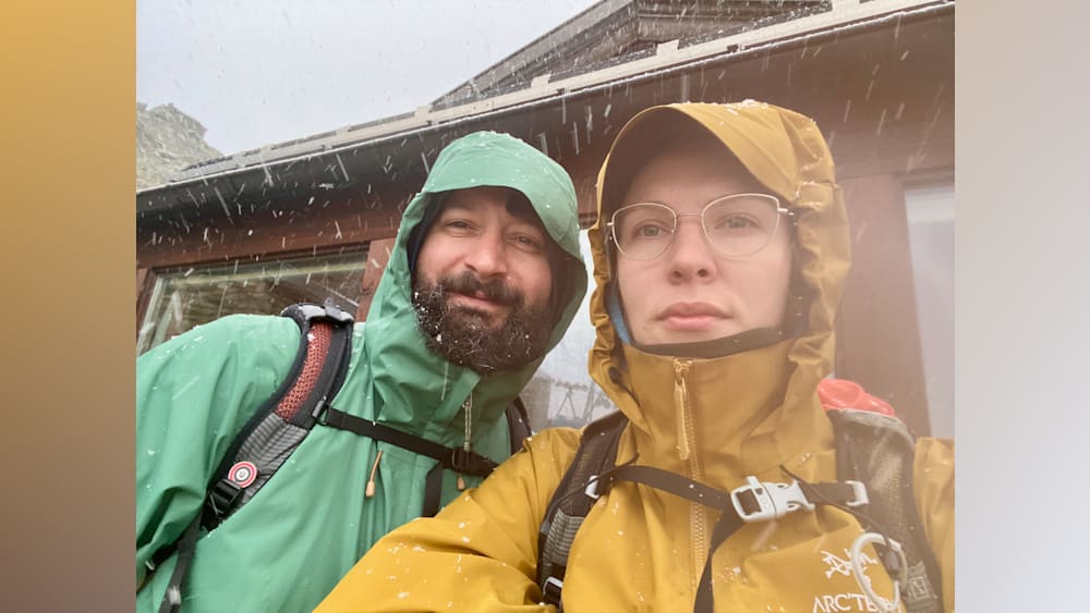 A man and a woman standing together in the rain, the woman is wearing glasses.