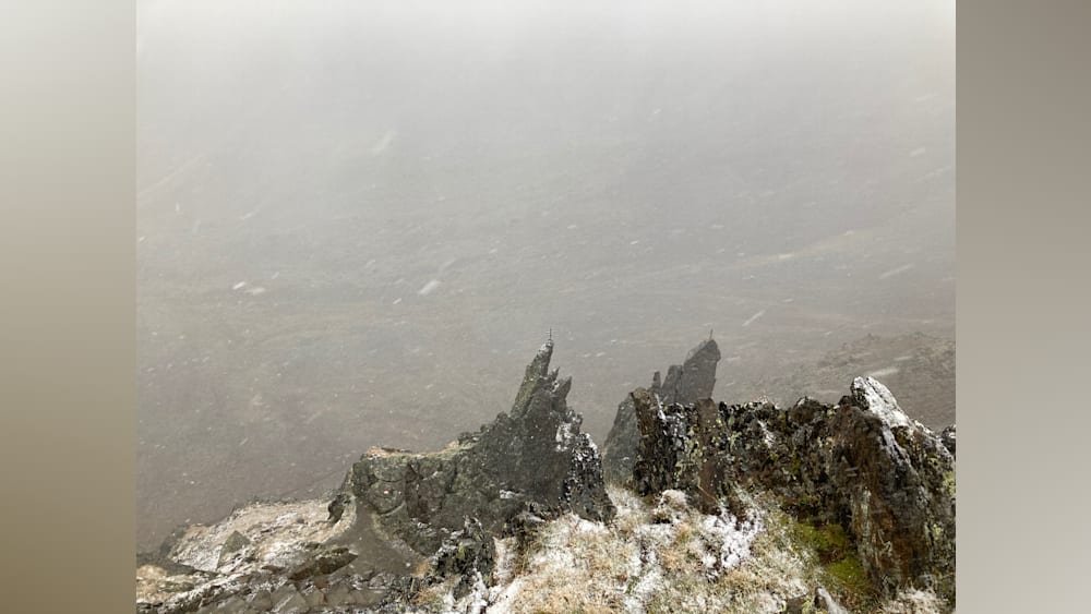 A foggy mountain peak with snow on the rocks below.