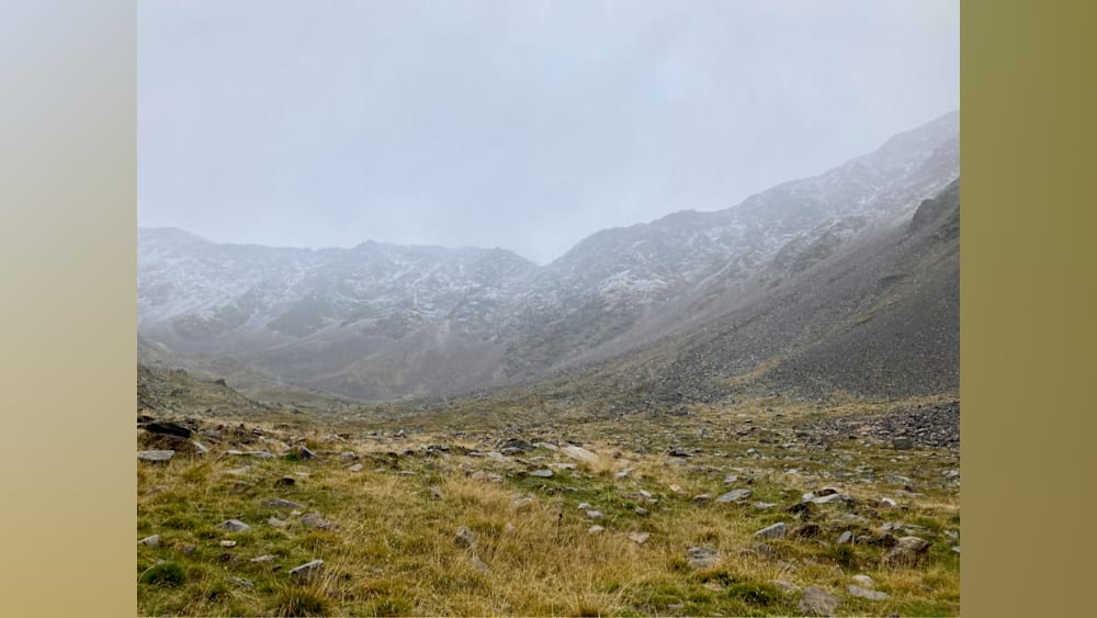 A rocky, grassy field with mountains in the distance.